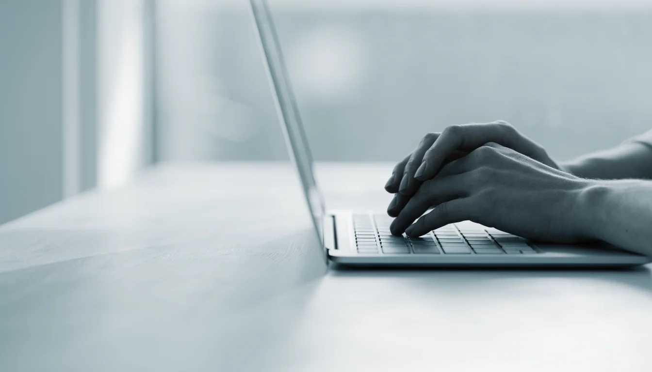 Hands resting on a laptop keyboard in a bright minimal office, pausing to think